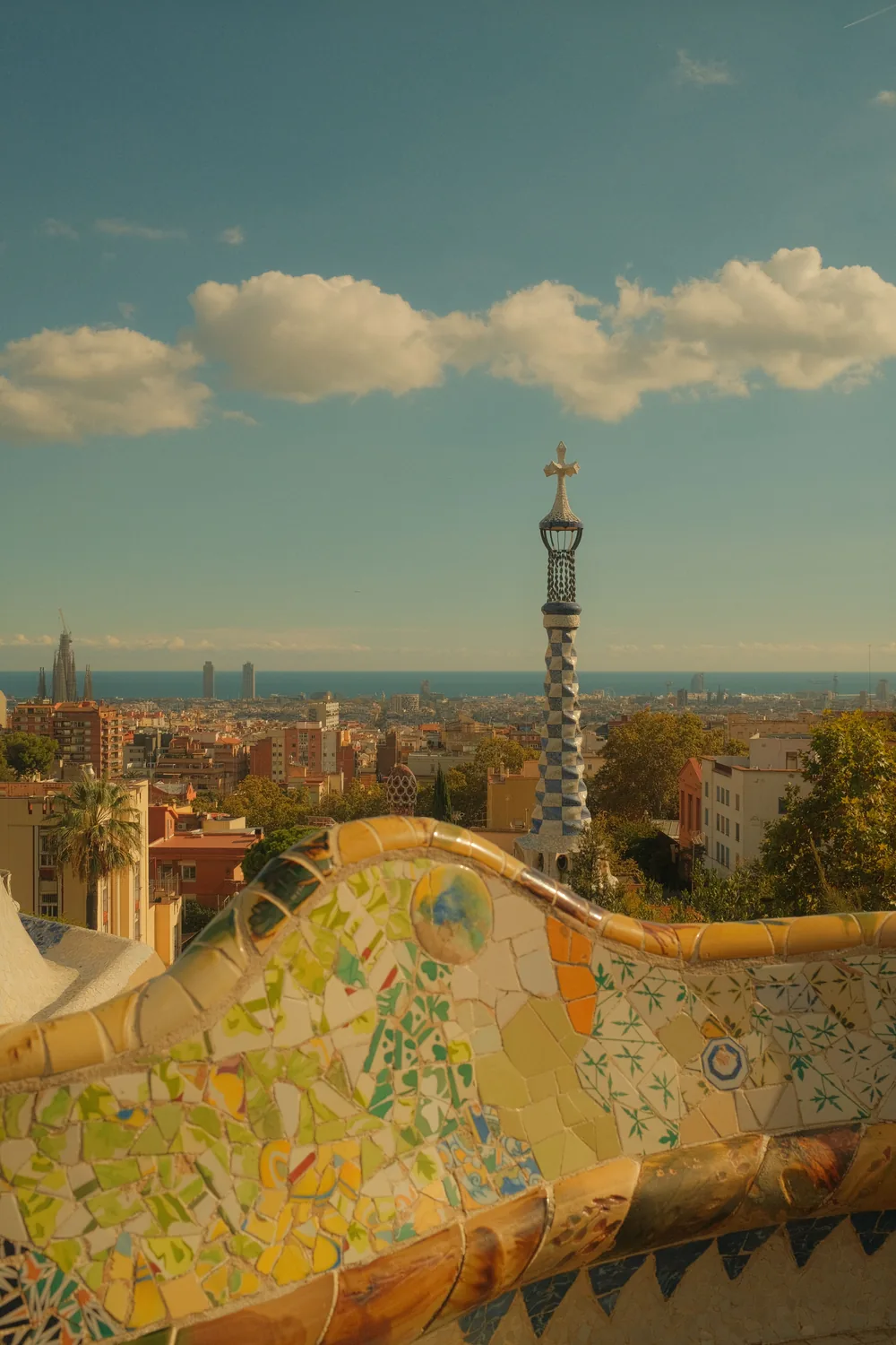 The mosaic terrace at Park Güell in late afternoon light, with Barcelona and the sea beyond