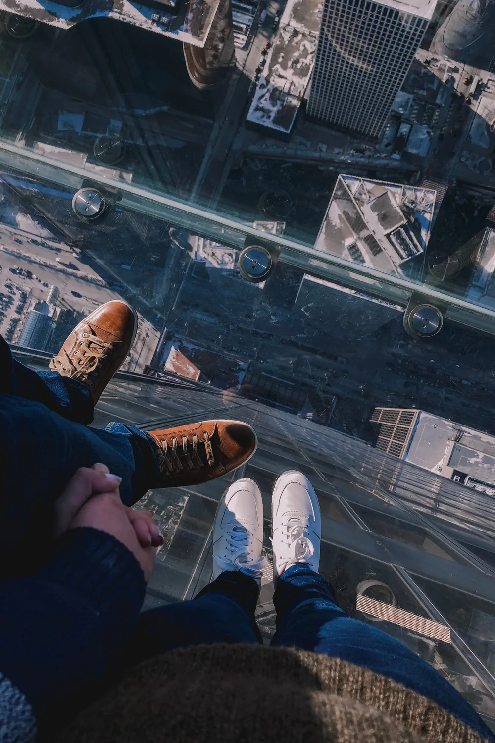 Looking down through the glass floor of the Willis Tower Skydeck ledge at the city far below, two people standing on it