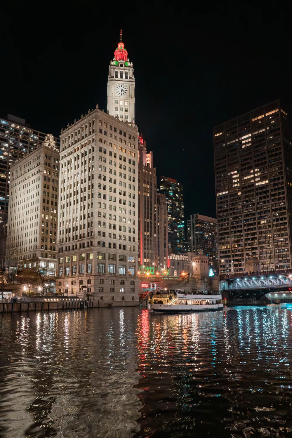 The Wrigley Building floodlit at night above the Chicago River, its lights reflected in the water