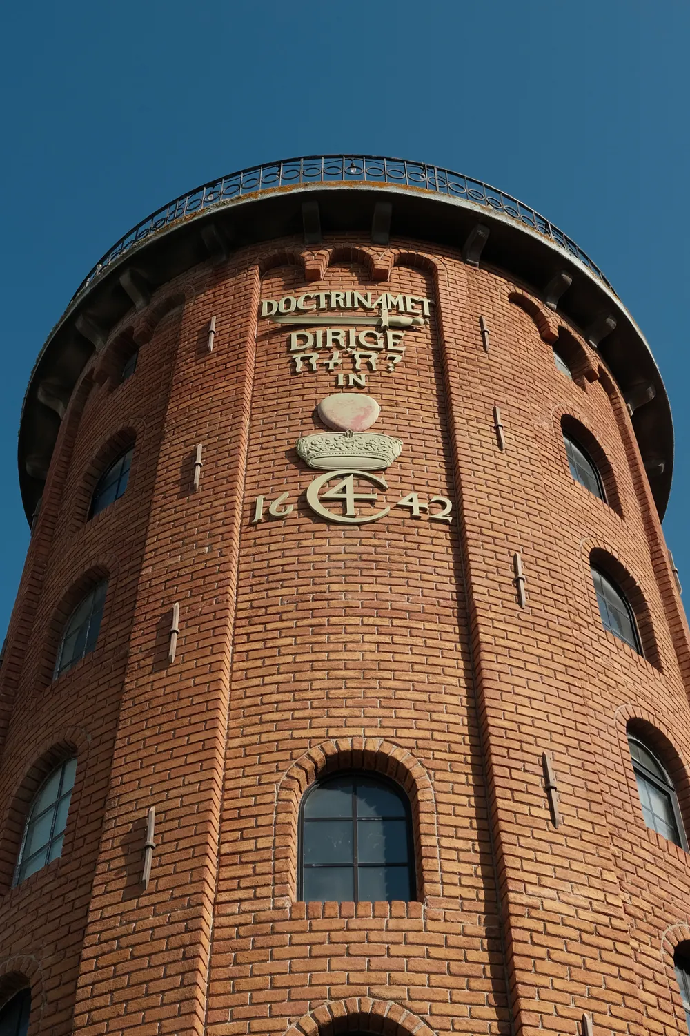 The Rundetaarn (Round Tower) in Copenhagen, its 17th-century brickwork and gilded 1642 rebus lit by low sun against a deep blue sky