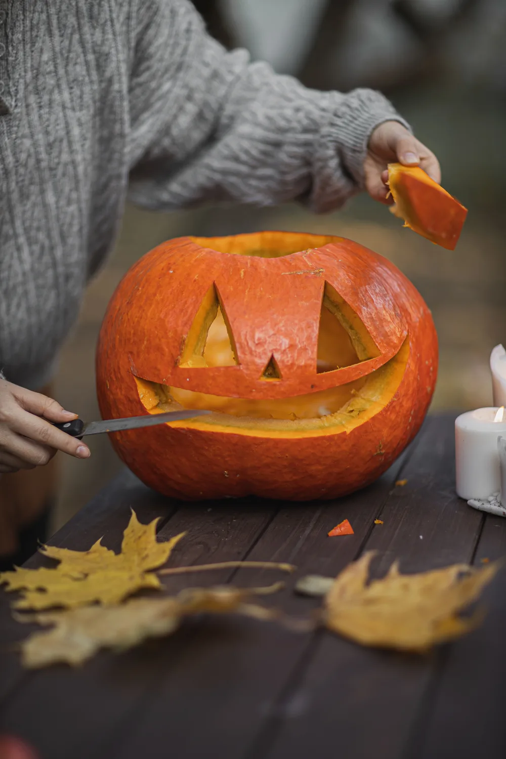 Hands carving a jack-o'-lantern face into a pumpkin on a wooden table