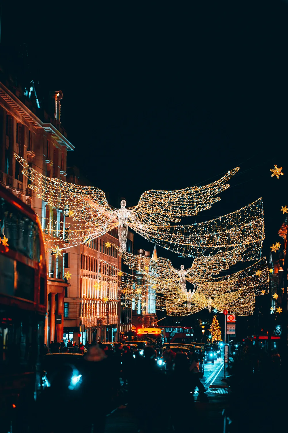 Illuminated angel Christmas lights strung high above a busy London street at night