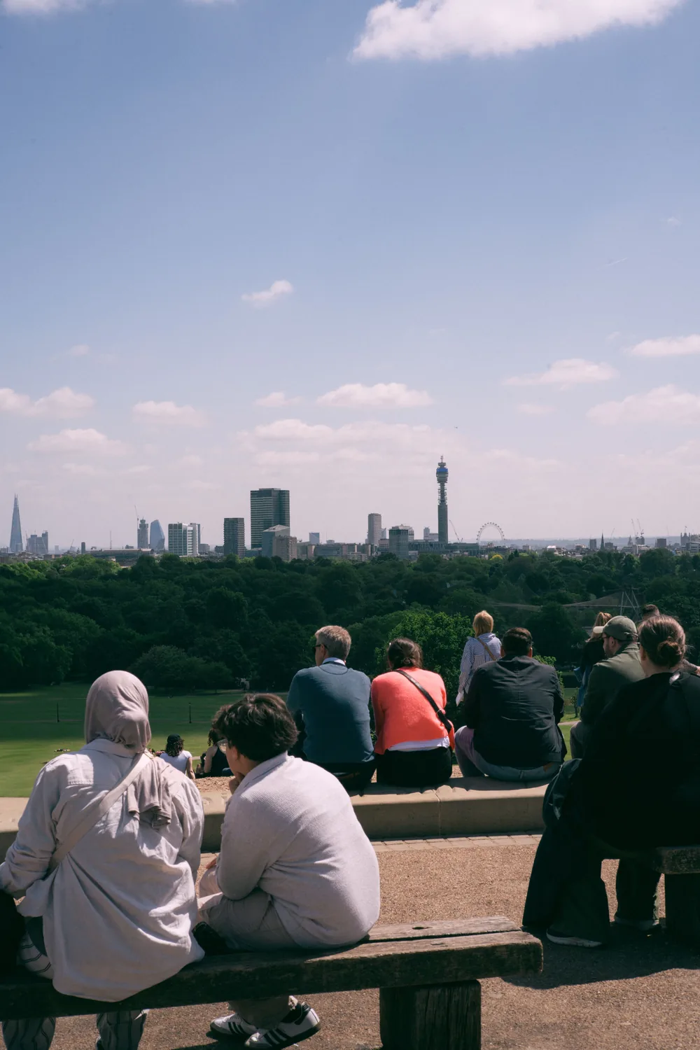 People sitting on a bench at the top of Primrose Hill looking out over the London skyline