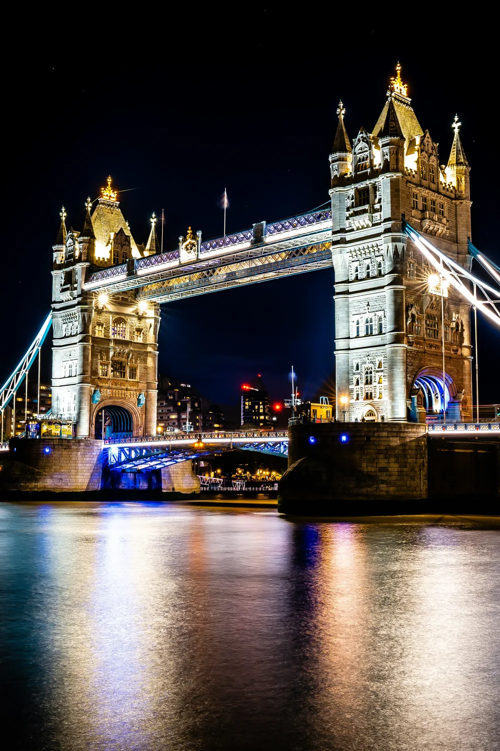 Tower Bridge lit gold at night, its lights reflected in the Thames below