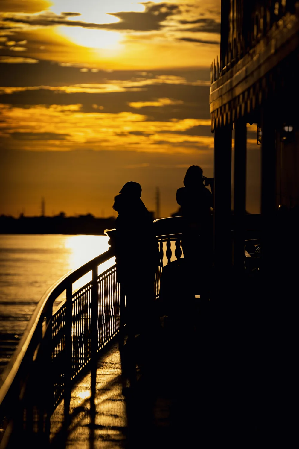 A couple silhouetted at the rail of a riverboat as the sun sets over the Mississippi