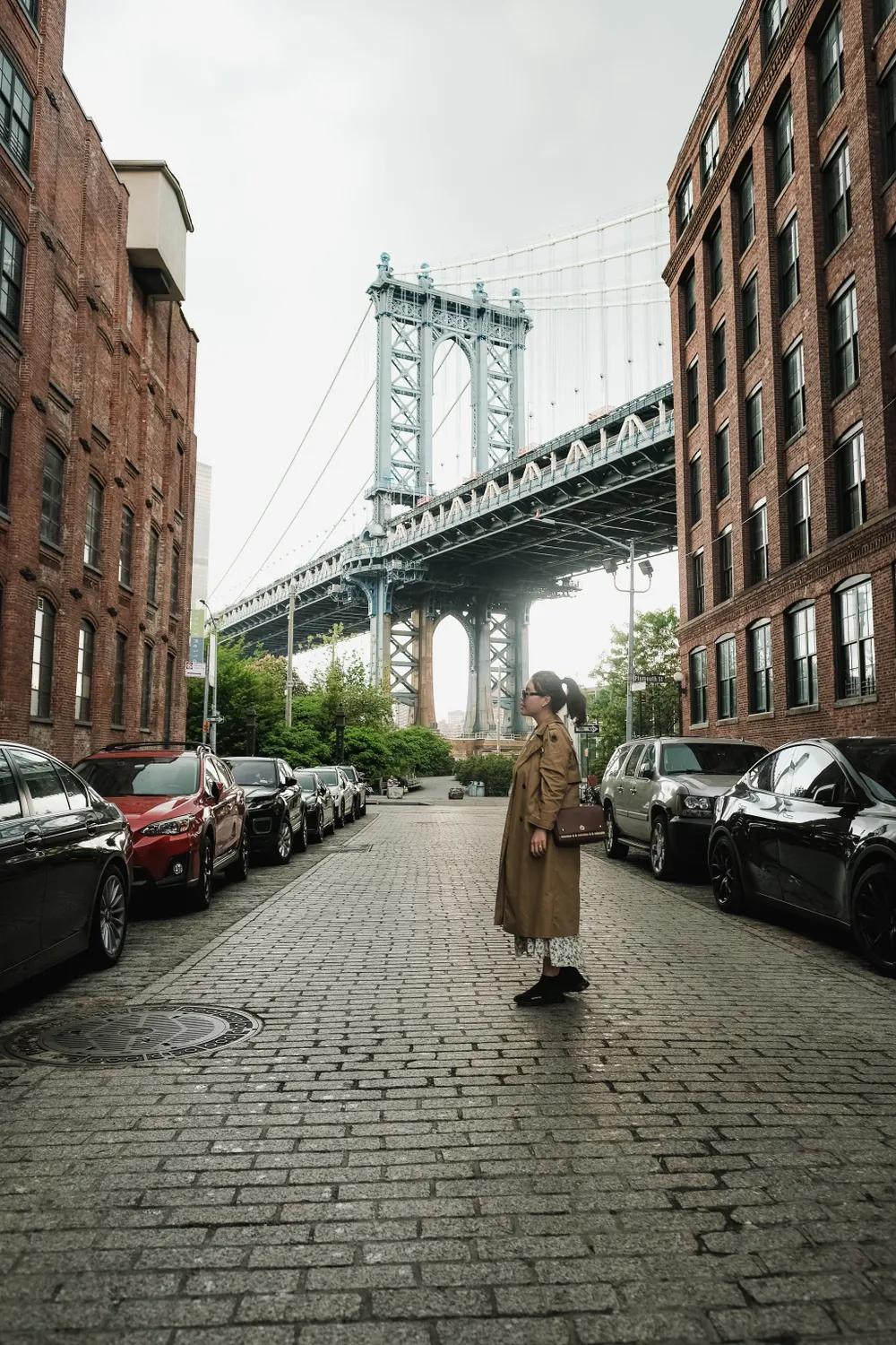 A cobblestone street in DUMBO framed by brick warehouses, the Manhattan Bridge crossing overhead