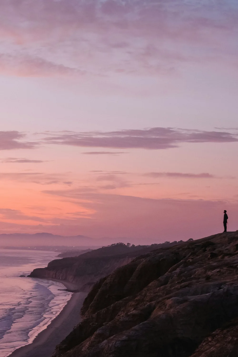 A figure standing on a bluff above the Pacific as the sky turns pink at dusk