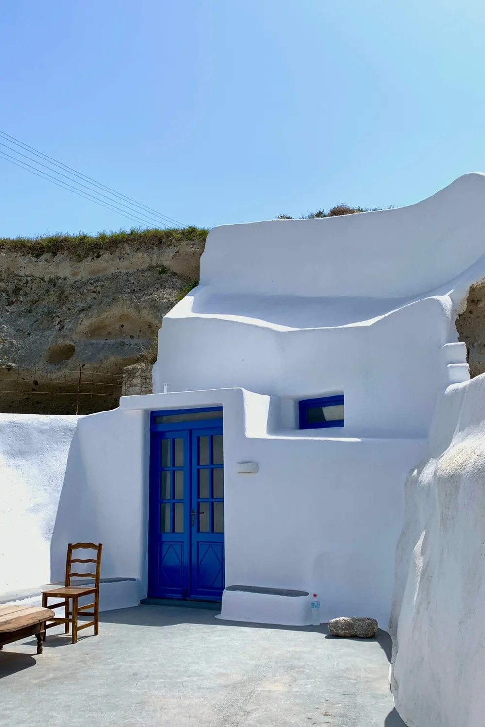 A whitewashed cave house in Megalochori with a vivid blue door and a single wooden chair outside
