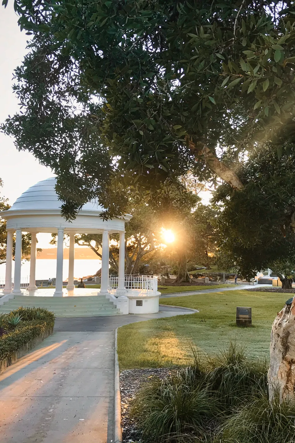 The white rotunda at Balmoral Beach at sunrise, with the sun breaking through the fig trees