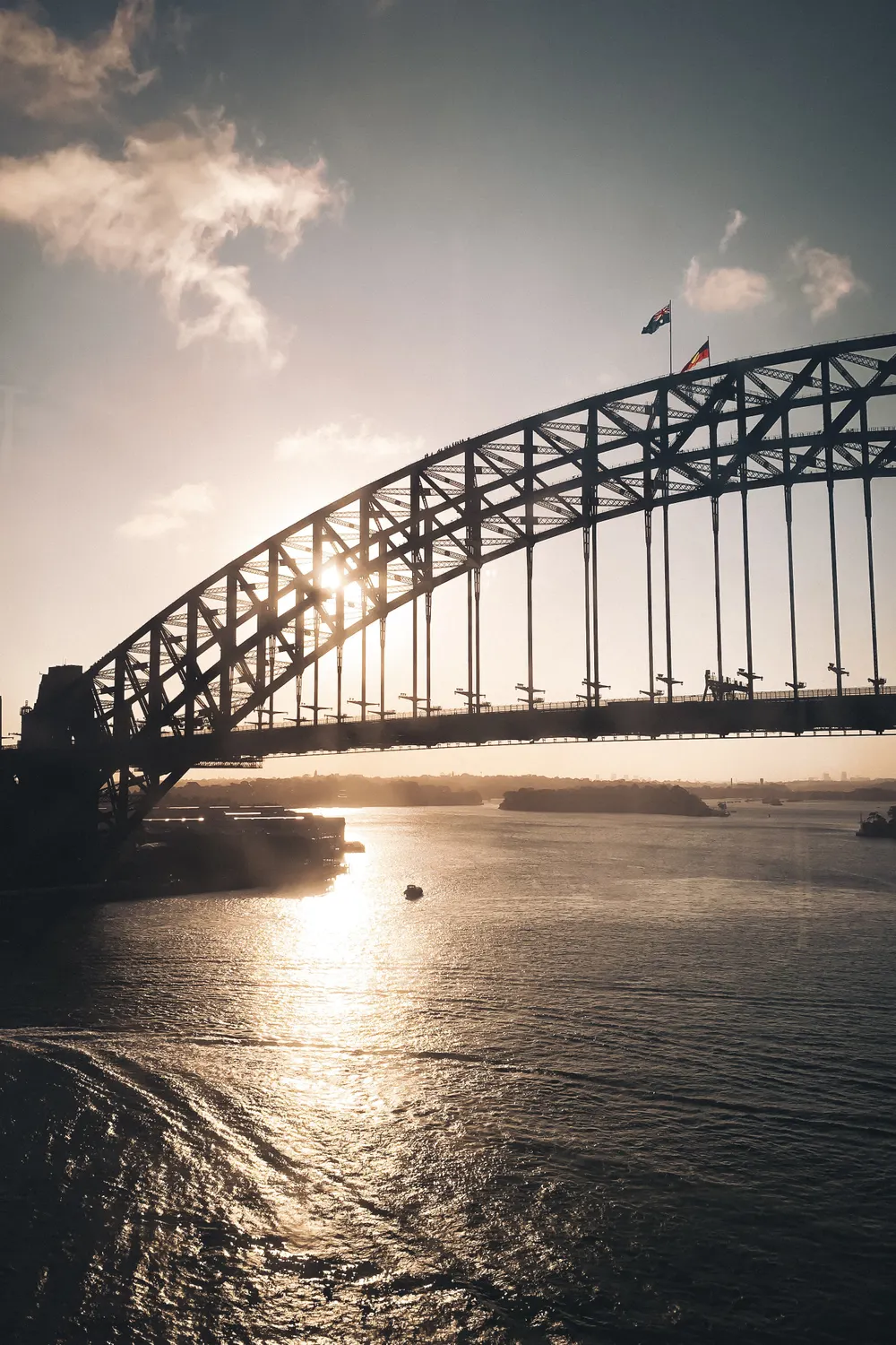 The arch of the Sydney Harbour Bridge silhouetted against the late afternoon sun, with climbers visible on the span
