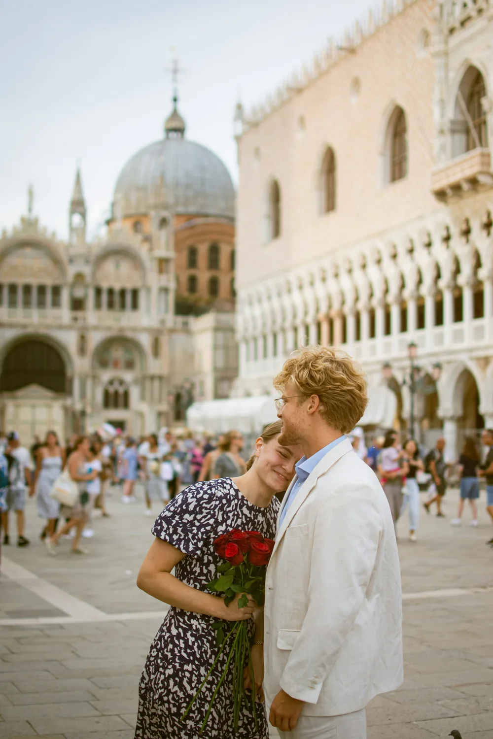 A couple holding red roses in the Piazza San Marco, the domes of St Mark's Basilica and the Doge's Palace behind them