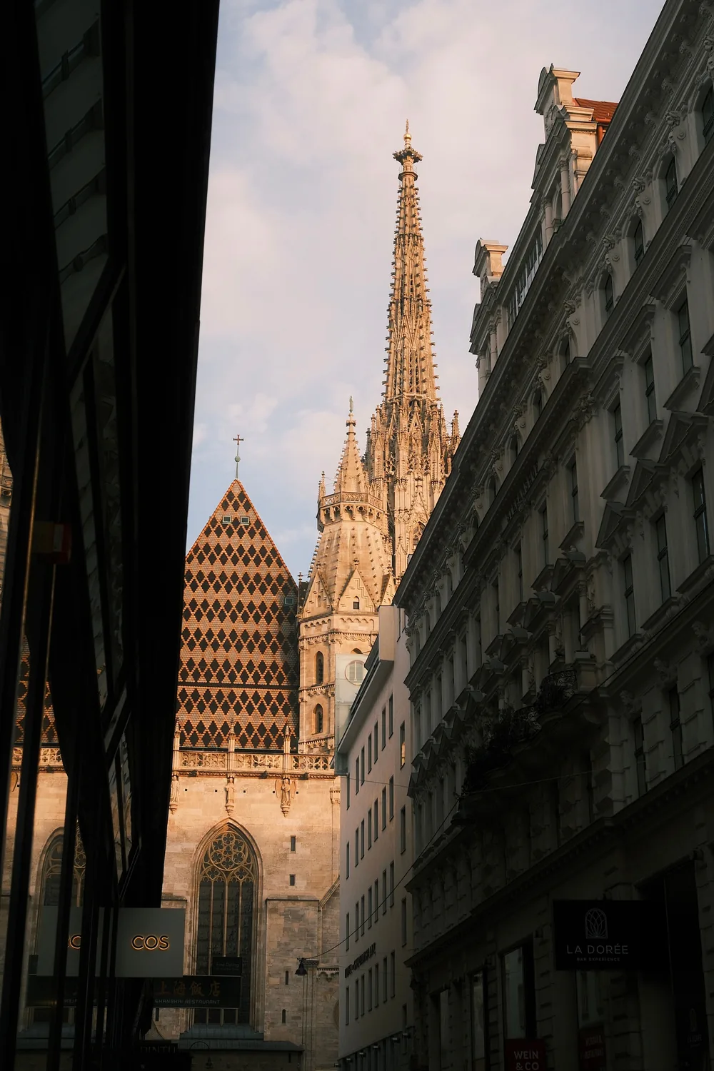The spire and patterned tile roof of St Stephens Cathedral seen between buildings on Stephansplatz