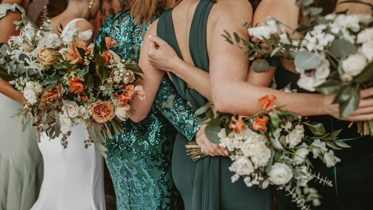 Bridesmaids in green dresses stand arm in arm holding bouquets