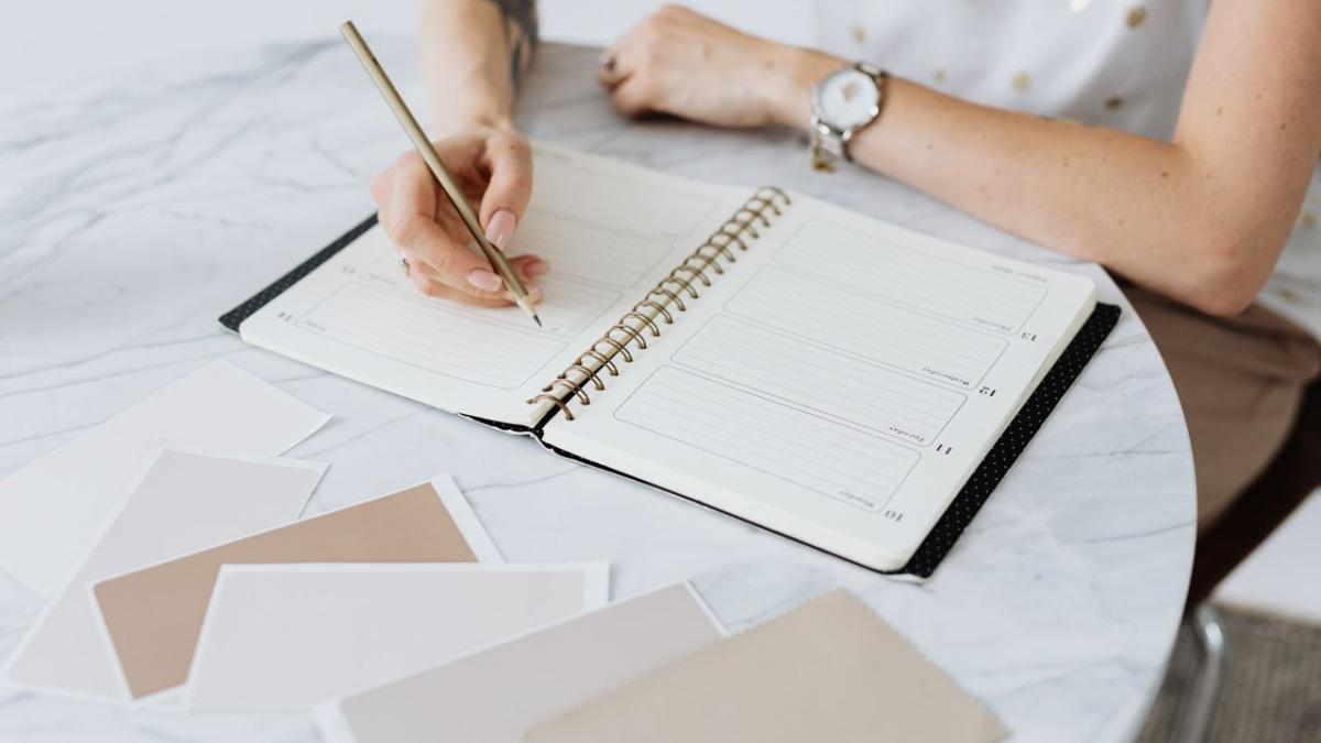 Hands writing in a planner beside colour swatches on a marble table
