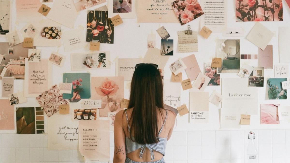 A woman studies a wall of pinned photos, swatches and cards in pinks and creams