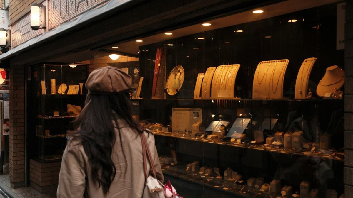 A woman in a beret looks into a lit jewellery shop window
