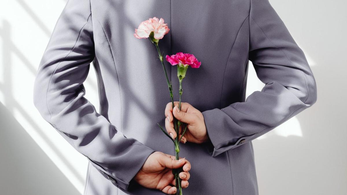 A man in a grey jacket hides two carnations behind his back