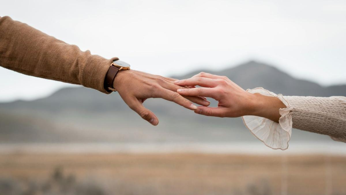 Two hands reach for each other with hills soft in the background