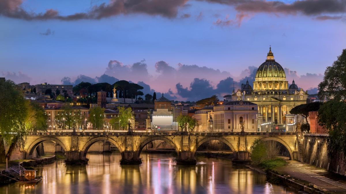 The skyline of Rome at twilight, with the illuminated dome of St Peter's above the Tiber