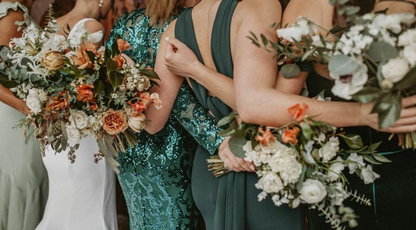 Bridesmaids in green dresses stand arm in arm holding bouquets