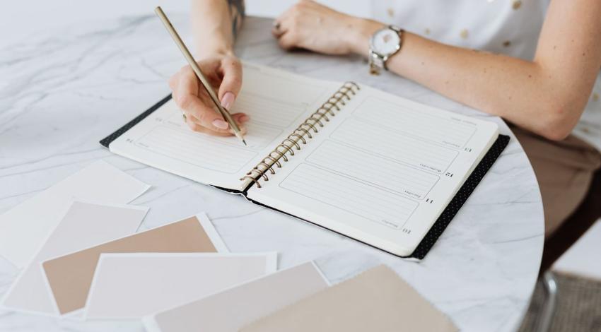 Hands writing in a planner beside colour swatches on a marble table