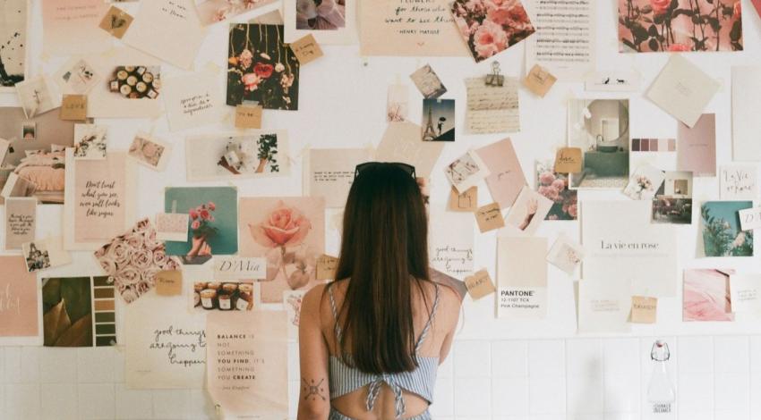 A woman studies a wall of pinned photos, swatches and cards in pinks and creams
