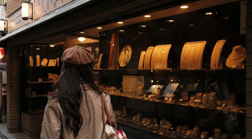 A woman in a beret looks into a lit jewellery shop window