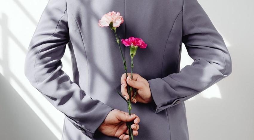 A man in a grey jacket hides two carnations behind his back