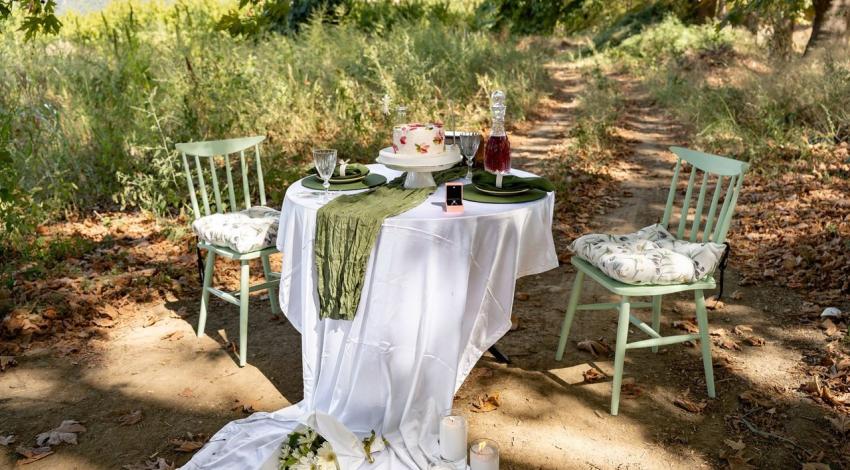 A table for two set with flowers and candles on a woodland path, waiting for the proposal