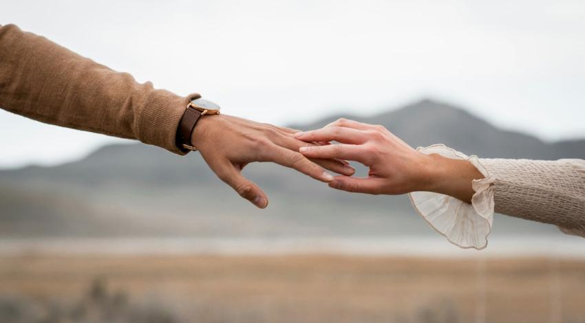 Two hands reach for each other with hills soft in the background