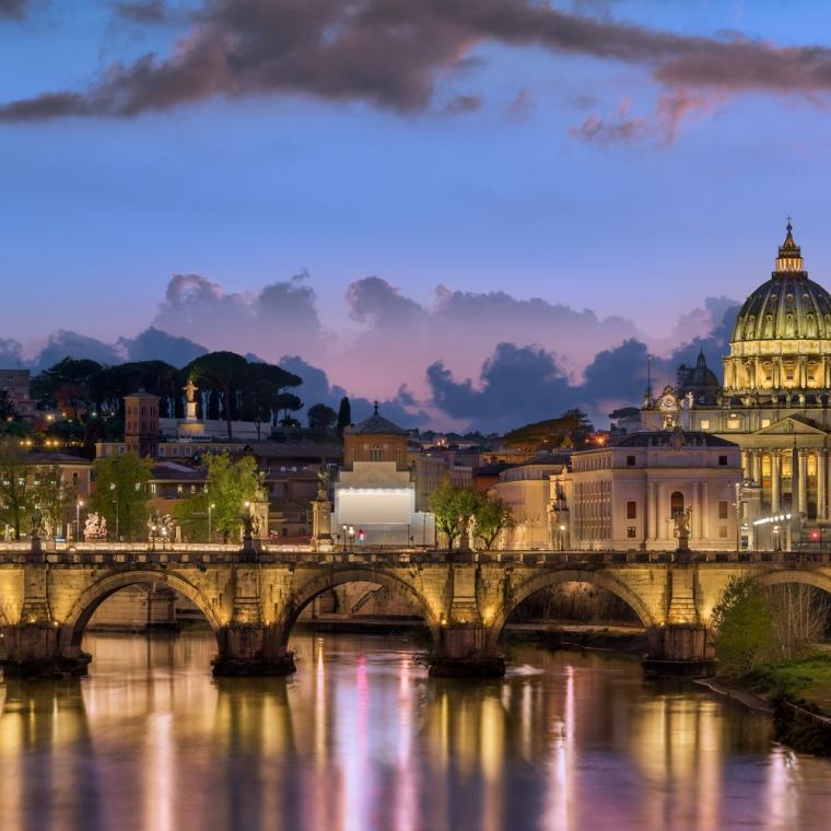 The skyline of Rome at twilight, with the illuminated dome of St Peter's above the Tiber