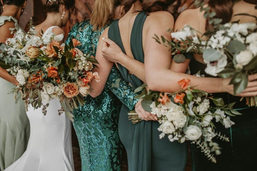 Bridesmaids in green dresses stand arm in arm holding bouquets