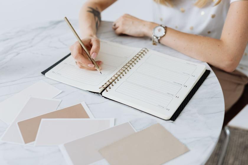 Hands writing in a planner beside colour swatches on a marble table