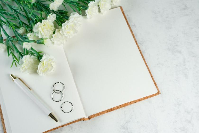 An open notebook, a pen, two rings and white carnations on marble