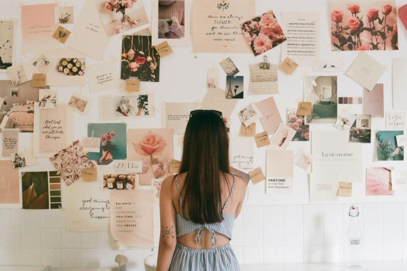 A woman studies a wall of pinned photos, swatches and cards in pinks and creams