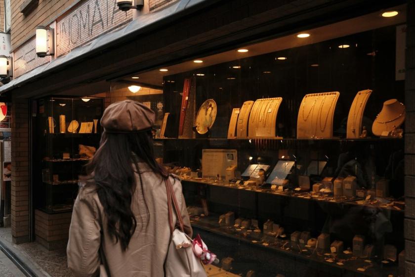 A woman in a beret looks into a lit jewellery shop window