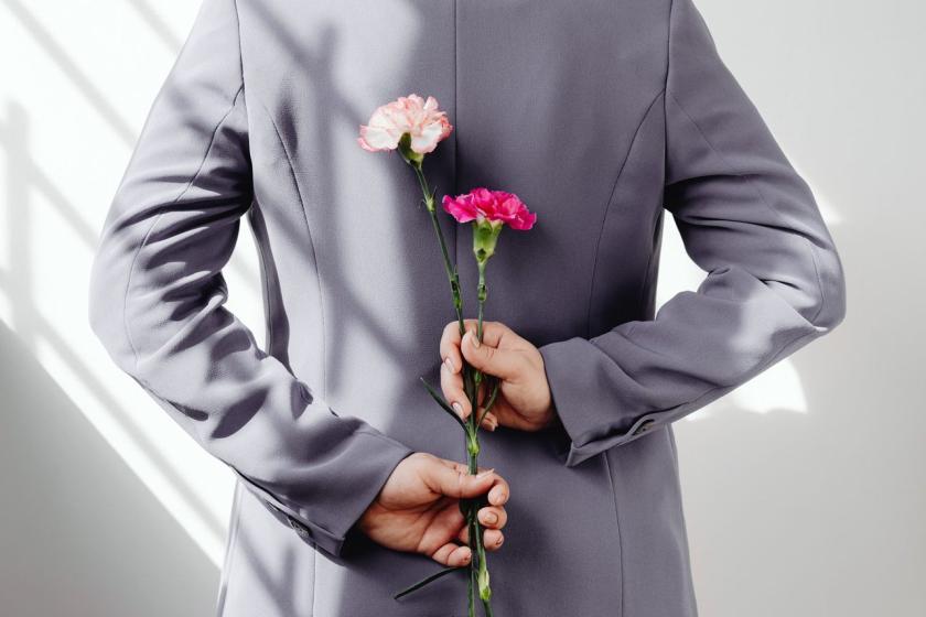 A man in a grey jacket hides two carnations behind his back