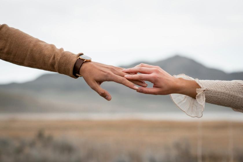 Two hands reach for each other with hills soft in the background