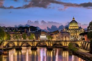 The skyline of Rome at twilight, with the illuminated dome of St Peter's above the Tiber