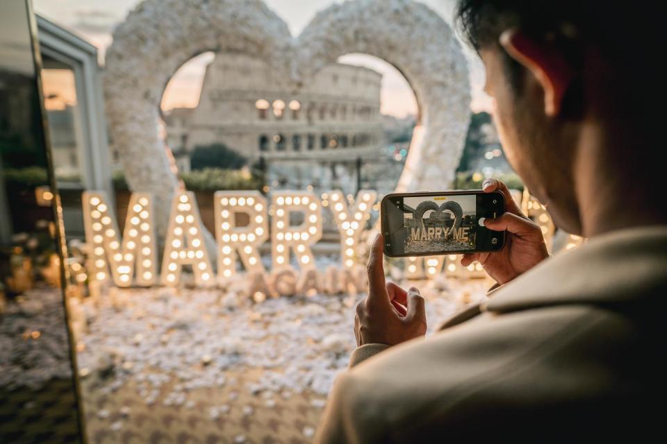Romantic marriage proposal setup with illuminated Marry Me letters overlooking the Colosseum in Rome, Italy