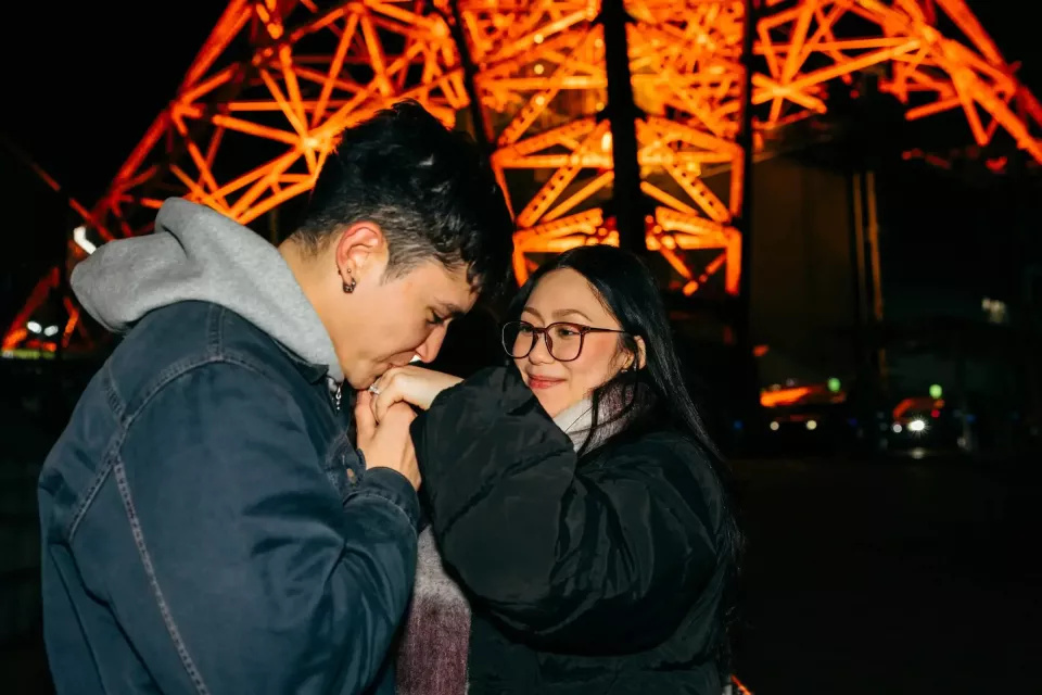 A couple under the lit orange frame of Tokyo Tower at night, just after the proposal