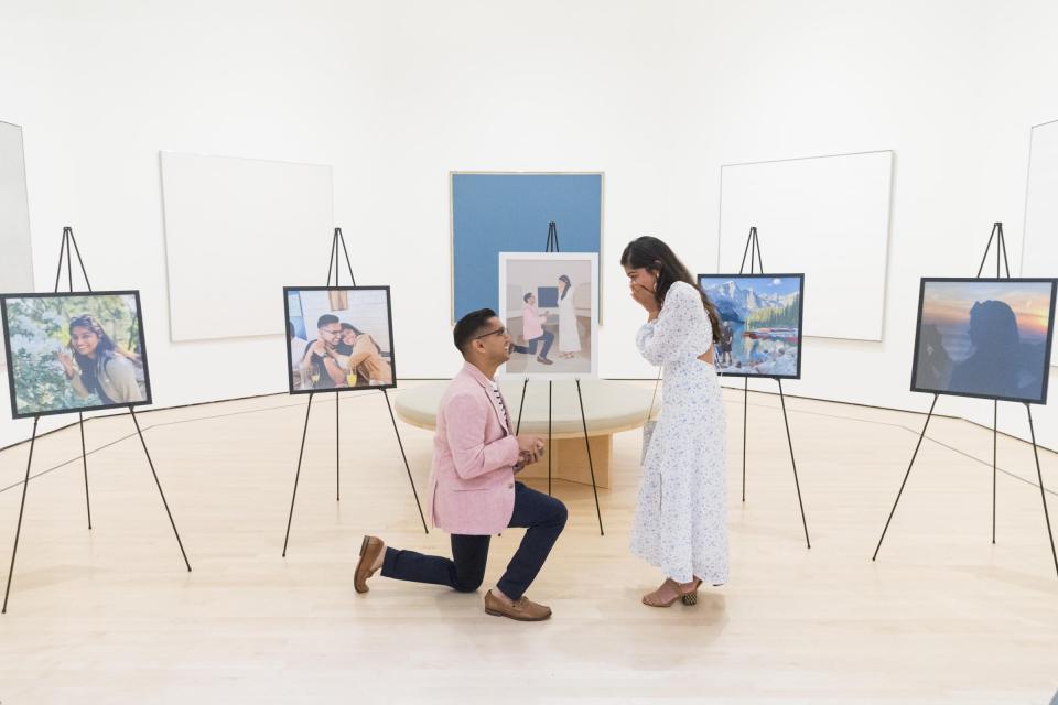 A proposal at SFMOMA inside a ring of easels holding framed photographs of the couple, with him kneeling in a pink blazer as she covers her face