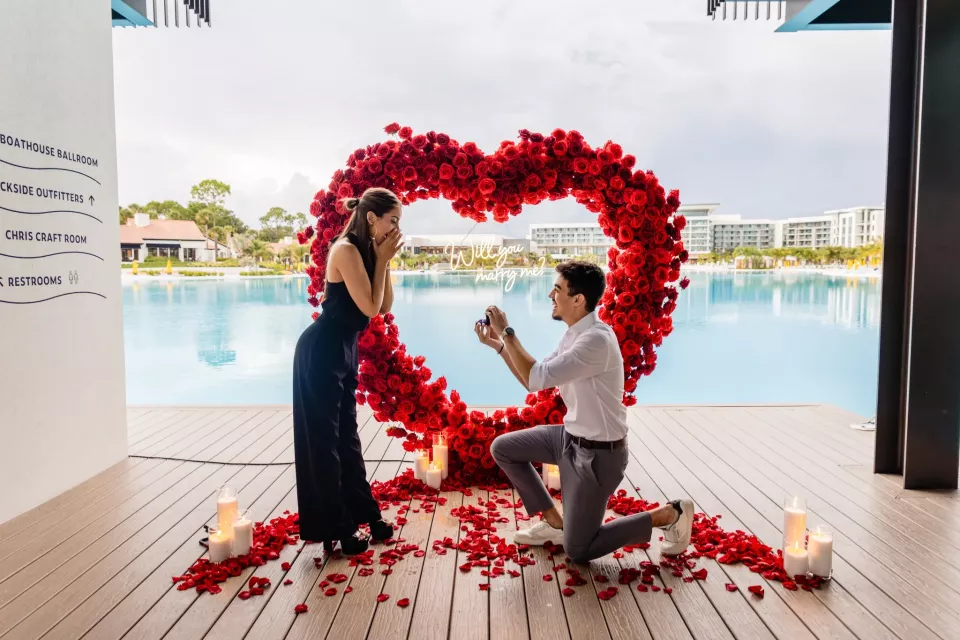 A proposal in front of a red rose heart arch beside a lagoon at Evermore Resort in Orlando
