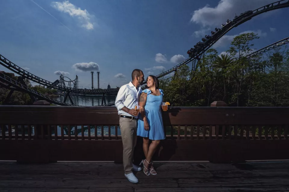 A couple stands together on a bridge with a roller coaster track curving overhead at Universal Orlando
