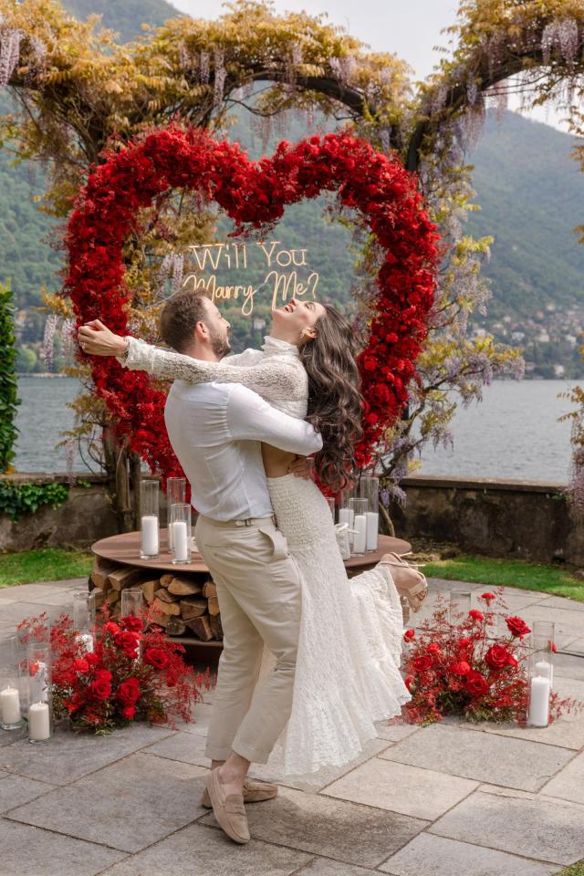 Couple celebrating their engagement beside a romantic heart-shaped floral proposal setup