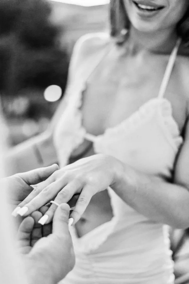 Close-up in black and white of an engagement ring being slid onto her finger moments after the proposal