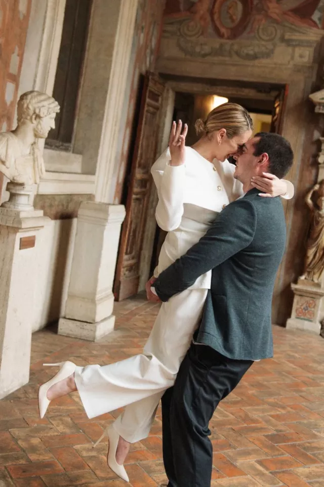 He lifts her off the ground in the frescoed loggia at Palazzo Altemps, just after she said yes