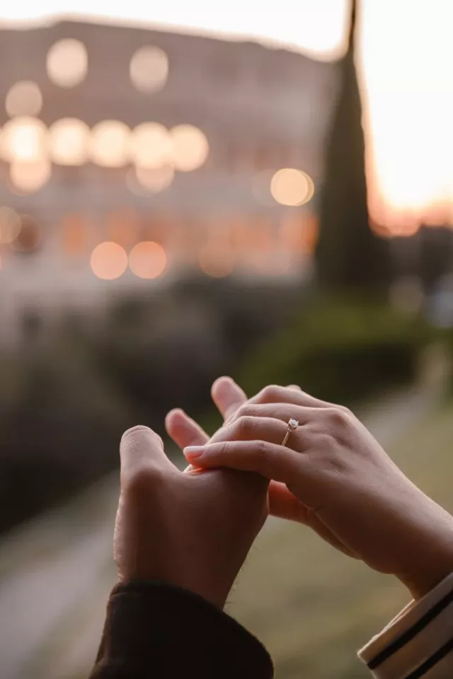 Her hand with the engagement ring held in his, the Colosseum lit behind them at sunset