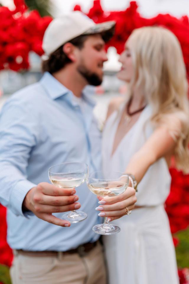 Newly engaged couple celebrating beside red rose proposal décor