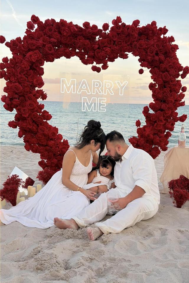 Couple seated inside a red rose heart arch on Miami Beach